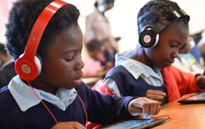 School kids wearing headphones while looking at tablet screens.